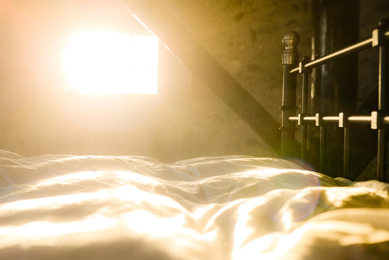Sunlight streaming through bedroom curtains onto a bed in the early morning