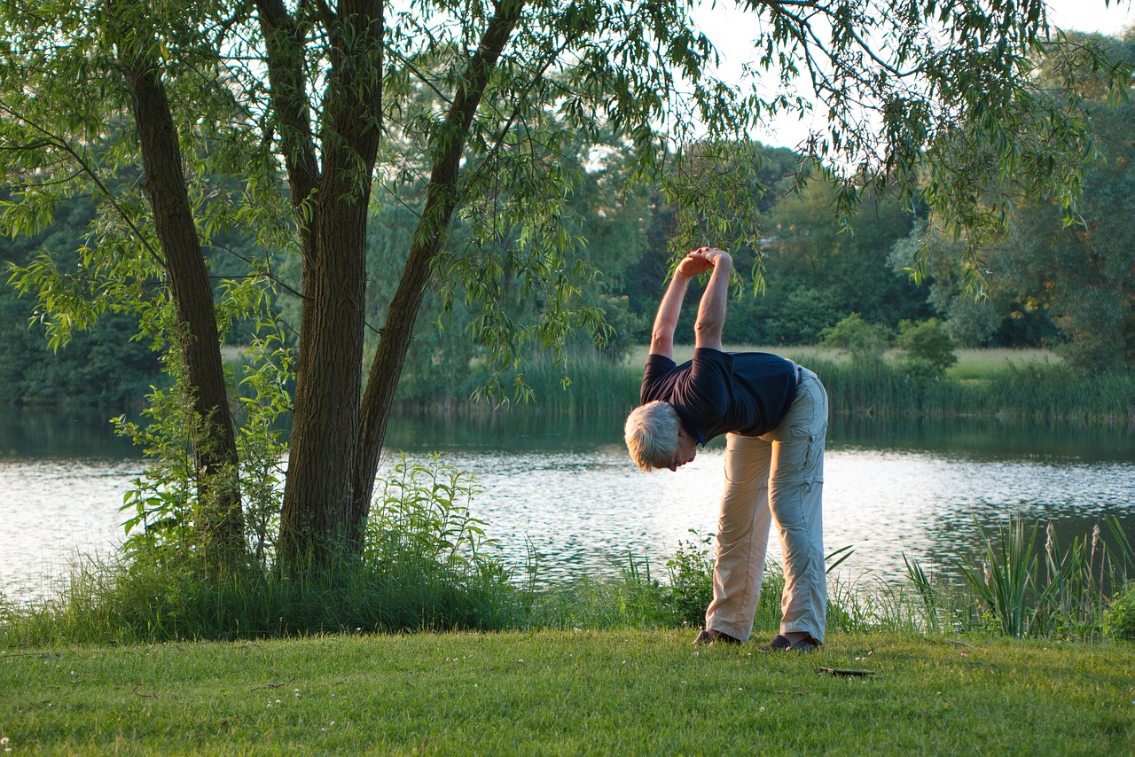 An older adult practicing outdoor yoga by a lake at sunrise, representing gentle, sustainable exercise during weight loss