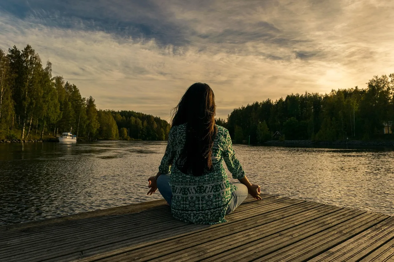 An older adult practices yoga outdoors by a lake at dusk, representing the physical activity that remains a foundation of cardiometabolic risk reduction