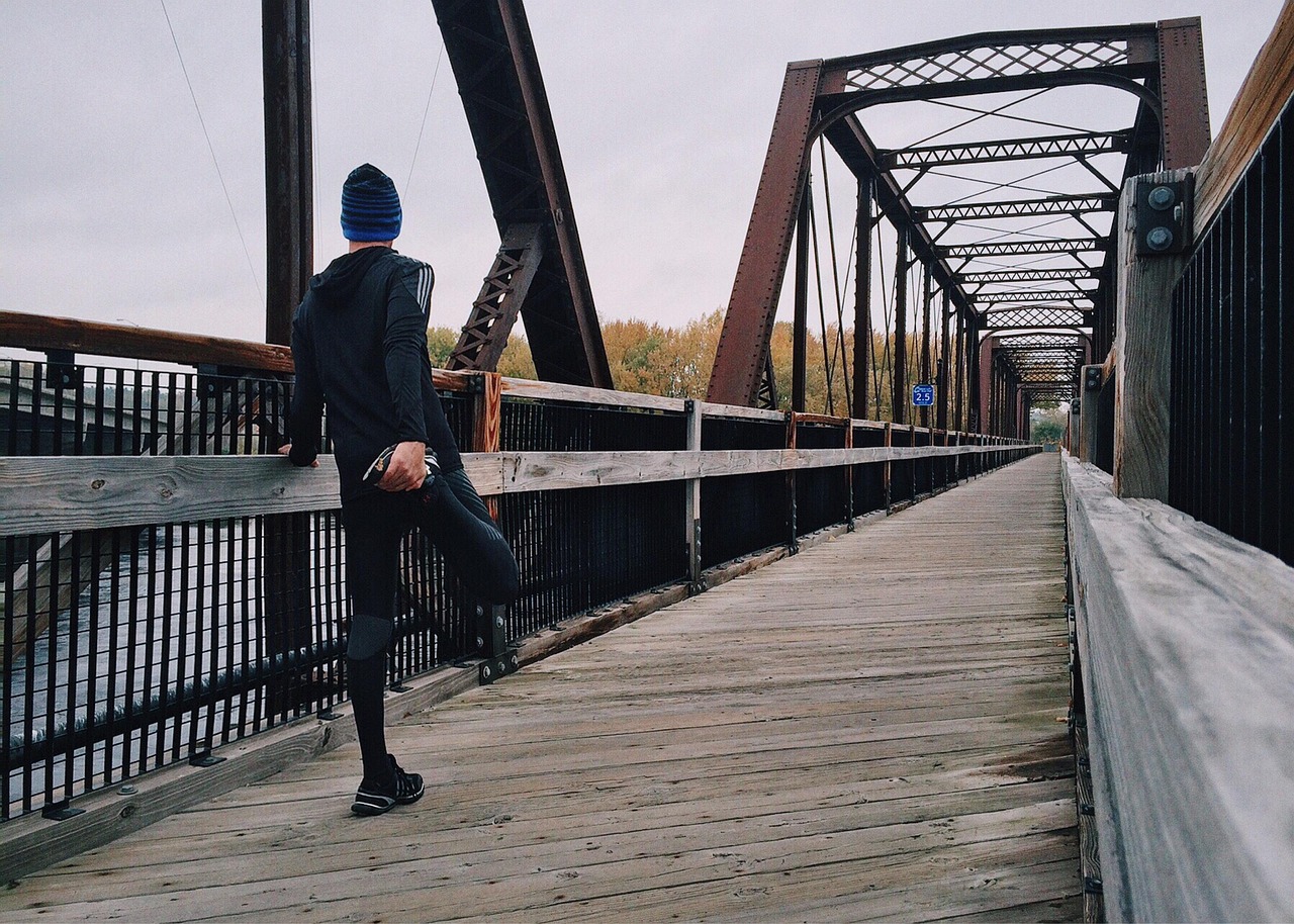 A runner pausing to stretch his leg against a railing on a pedestrian bridge, a simple recovery habit often paired with compression garment use