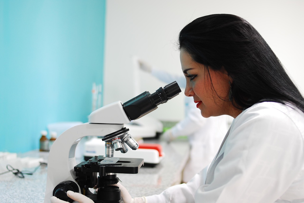 Researcher examining a sample through a laboratory microscope, representing the study of myostatin signaling in muscle biology
