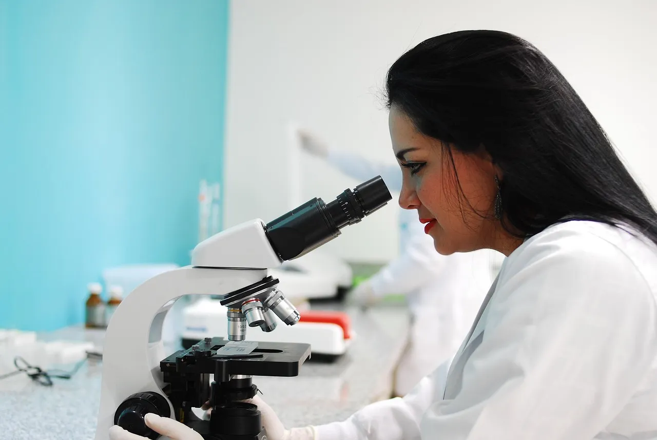 Researcher examining a sample through a laboratory microscope, representing the study of myostatin signaling in muscle biology
