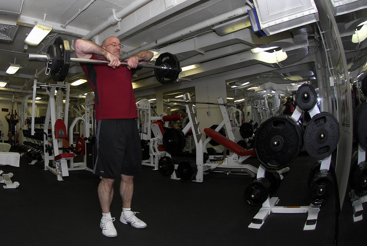 An older adult using cardio and strength equipment in a gym, illustrating the resistance training component of multicomponent exercise programs